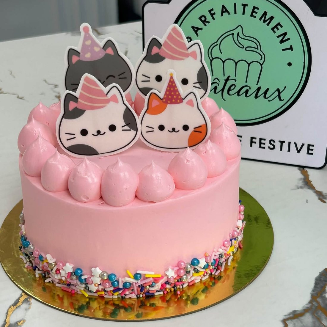 Un gâteau rose avec des figurines de chats et des confettis sucrés