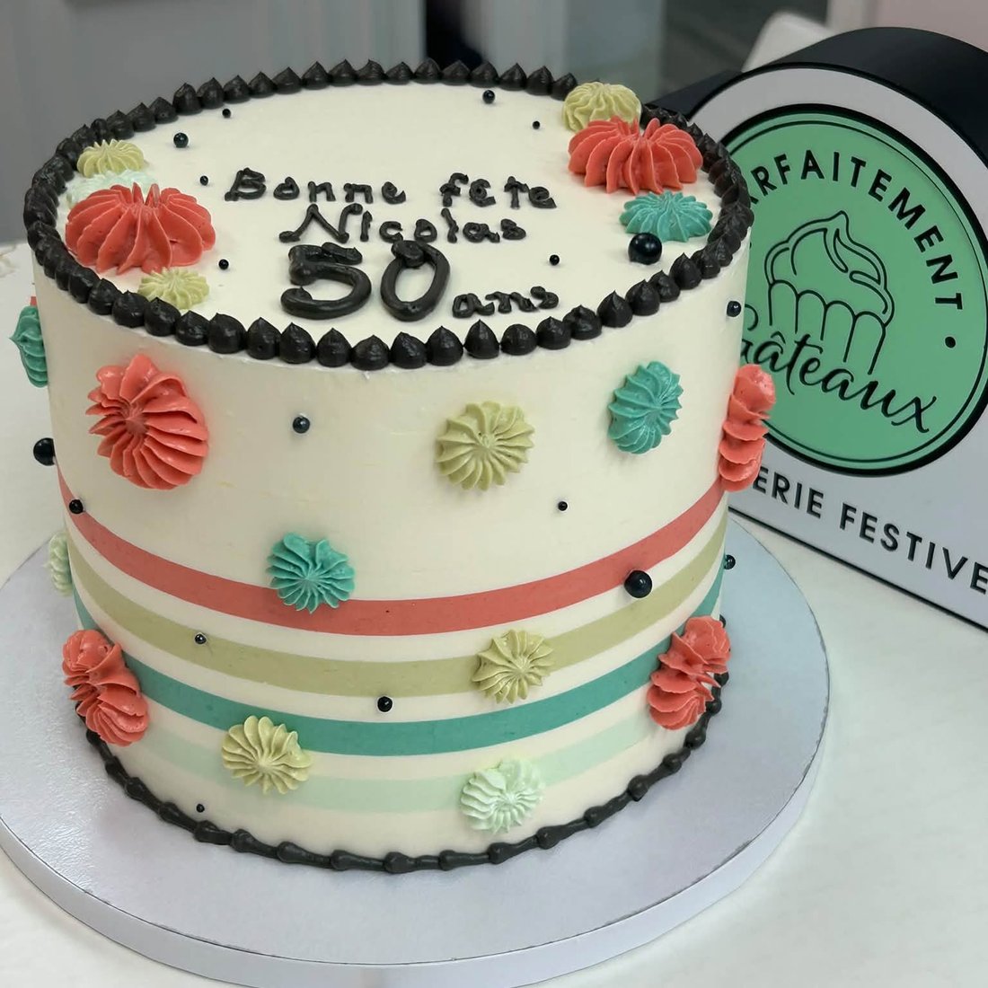 Un gâteau d’anniversaire rayé, décoré de rosettes corail et menthe