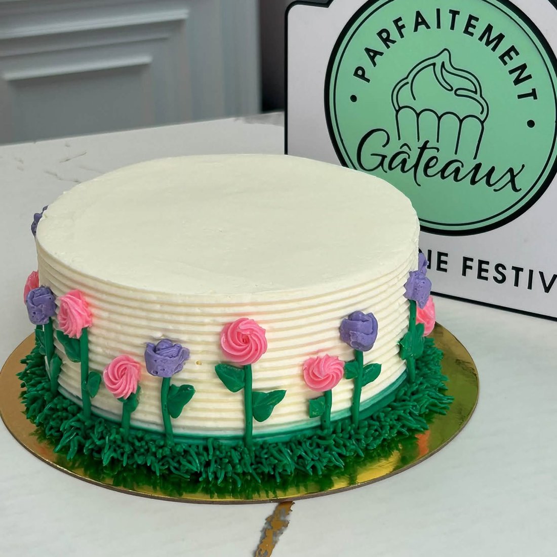 Un gâteau blanc ceinturé de fleurs piquées à la poche sur un gazon de crème