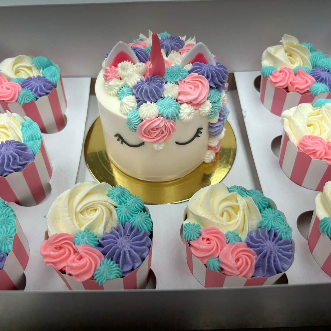 Un gâteau licorne entouré de cupcakes à rosettes