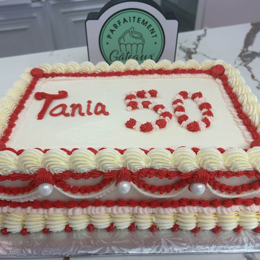 Un gâteau rectangulaire au glaçage rouge portant le prénom Tania